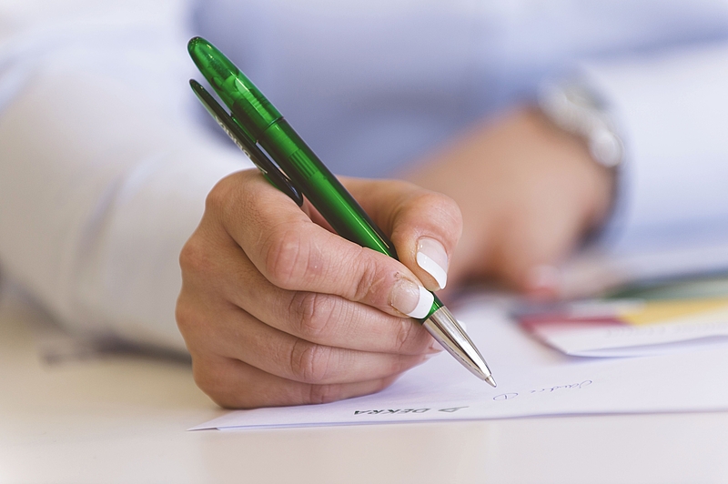 eine Hand hält einen Stift und schreibt auf ein Blatt Papier